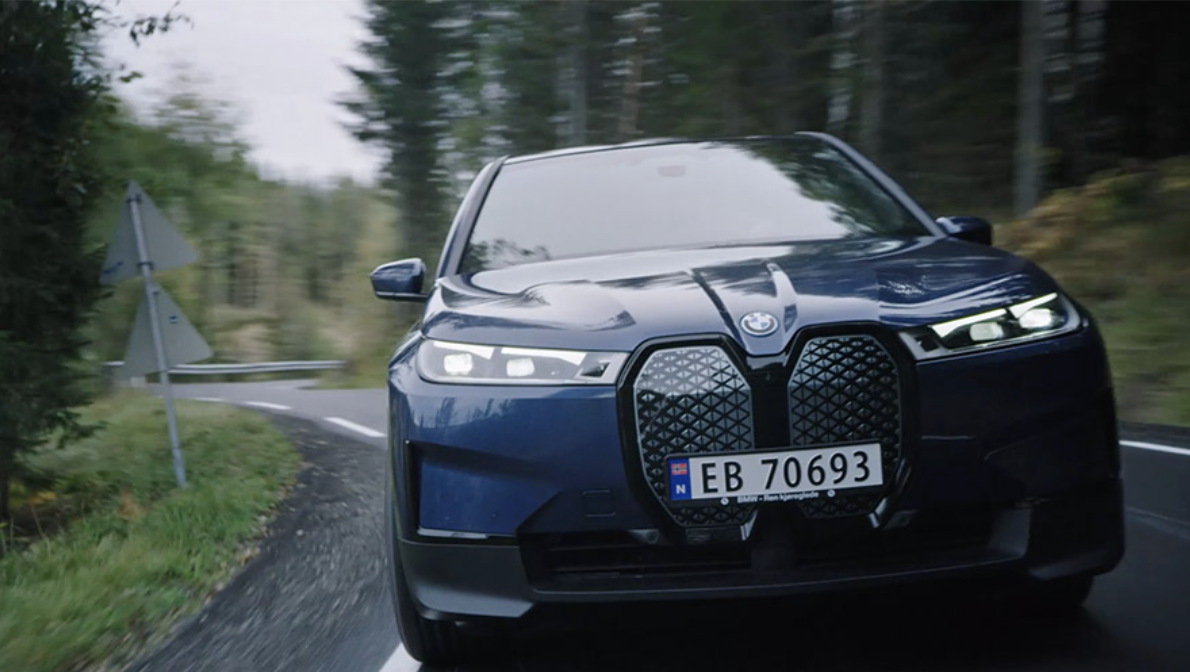 BMW iX fährt auf einer ländlichen Küstenstraße an einem Berghang entlang